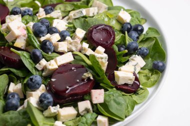 Ispanaklı, pancarlı, mavi peynirli ve susamlı lezzetli bir vejetaryen salatasıyla büyük beyaz bir tabak. Güzel servis edilmiş yemek. Sağlıklı beslenme. yiyecek arka planı.