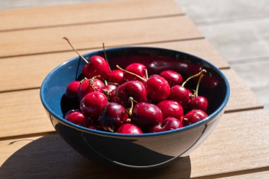 Güneşli bir yaz gününde, ahşap bir arka planda mavi bir kasede kırmızı, lezzetli kirazlar, hayat aşığı yaşam tarzı, metnin için yer, alıntılar için arka plan.