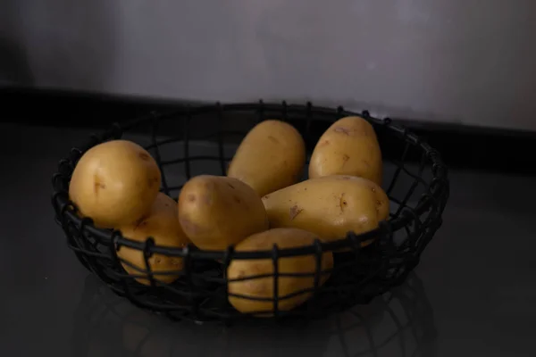 Fresh potatoes in a black metal basket on a black kitchen table. Food advertisement, kitchen poster, space for your text.