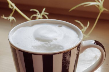 Siyah ve beyaz çizgili kahve kupası. Güneşli bir yaz sabahında, ahşap bir pencere eşiğinde kahve ve süt köpüğü. Bir yudum..