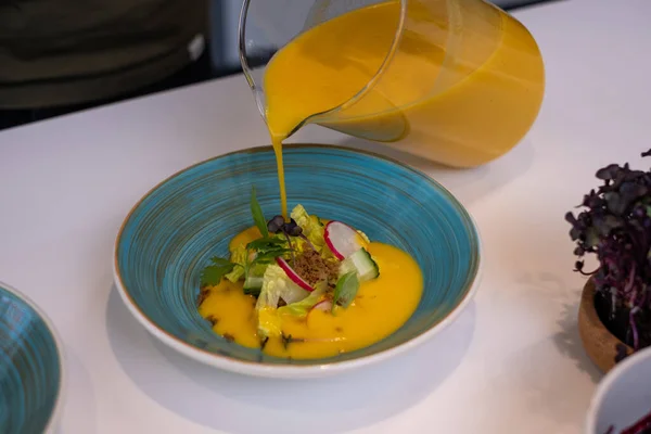 blue plates with greens and vegetables, and bright yellow tomato soup. Healthy food advertisement, kitchen background.