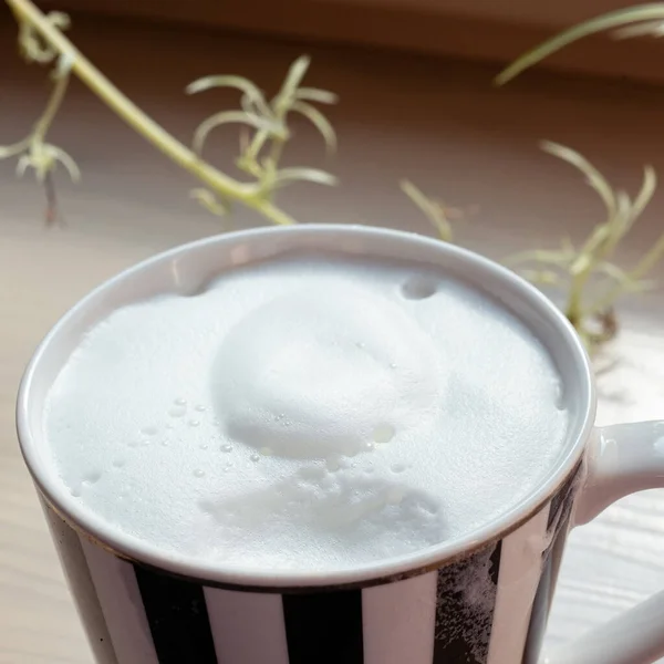 夏日的一个阳光明媚的早晨 白色和黑色条纹咖啡杯 上面有咖啡和牛奶泡沫 放在木制窗台上 一小口 — 图库照片