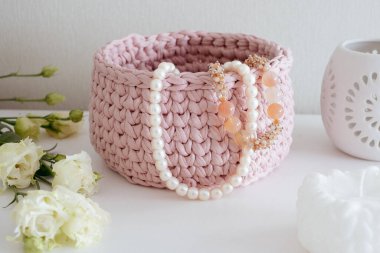 İnci kolye ve boncuklar pembe bir sepetin içinde beyaz bir masa üzerinde beyaz bir iç kısımda. Sıcak ev atmosferi, el işi reklamı.