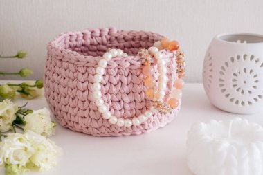 İnci kolye ve boncuklar pembe bir sepetin içinde beyaz bir masa üzerinde beyaz bir iç kısımda. Sıcak ev atmosferi, el işi reklamı.