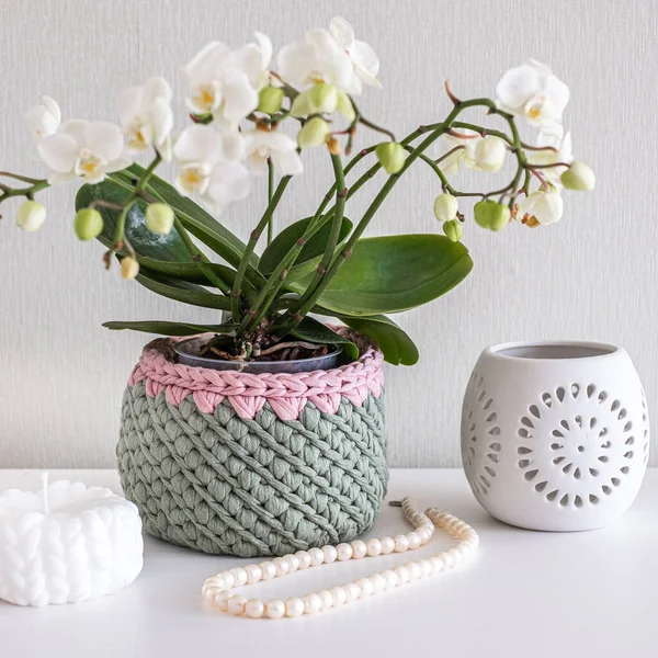 Pembe örgü sepetinde inci kolye ve boncuklar, beyaz mum, mum tutacağı ve lisianthus buketi beyaz iç tarafta beyaz masada. Sıcak ev atmosferi, el işi reklamı.