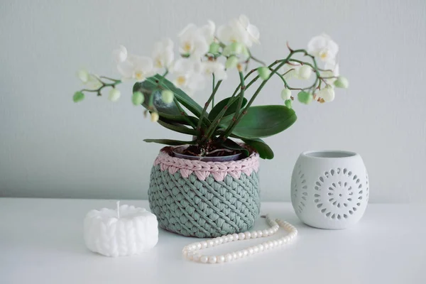 Pembe örgü sepetinde inci kolye ve boncuklar, beyaz mum, mum tutacağı ve lisianthus buketi beyaz iç tarafta beyaz masada. Sıcak ev atmosferi, el işi reklamı.