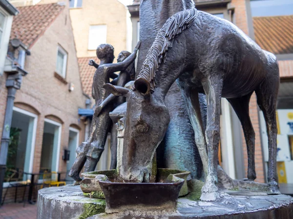 The sculpture of a horse drinking water in front of a lovely couple on a street in Bruges, Belgium.