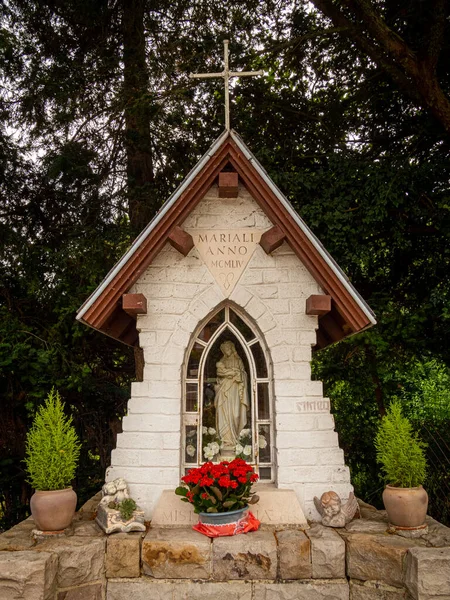 Small pilgrimage rural chapel of Virgin Mary made of stone, Stockel, Brussels, Belgium. Red flowers are placed in front of Mary.