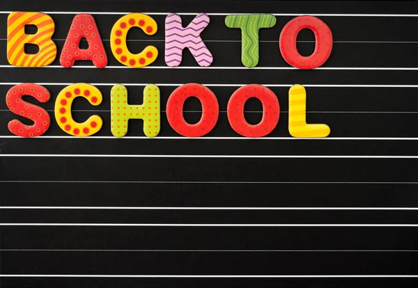 Back to school concept with colorful magnetic letters on a chalkboard as a black background. There is a free text field.