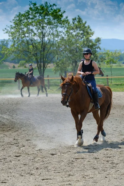 Two girls with helemts are riding horses at a riding school