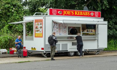 Basingstoke, İngiltere - 3 Temmuz 2021: Müşteriler bir yaz akşamı Basingstoke, Hampshire 'da park halindeki Joe' s Kebabs minibüsünde yemek bekliyor.