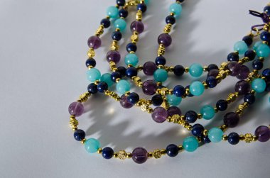 Mor ametistten yapılmış bir kolyenin bobinleri, mavi lapis lazuli ve turkuaz değerli taşlardan yapılmış. Düşen gölgesi olan beyaz bir arkaplanda görüntülenir.