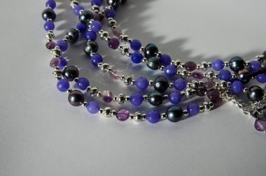 Tatlı su kültürü incilerden yapılmış el yapımı kolye, ametist ve gümüş kaplama bulgularla dizilmiş kuvarsit boncuklar. Düşen gölgeli beyaz bir arkaplanda fotoğraflanmış.