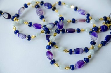 Altın kaplamalı boncuklarla süslenmiş ve beyaz bir yüzeye sarılmış mavi kuvars ve mor akik boncuklardan yapılmış bir kolye..