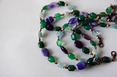 Beyaz bir zemin üzerine sarılı el yapımı bir kolye. Aquamarine ve agate değerli taşlarından yapılmış..  