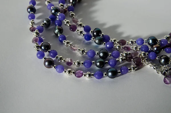 Tatlı su kültürü incilerden yapılmış el yapımı kolye, ametist ve gümüş kaplama bulgularla dizilmiş kuvarsit boncuklar. Düşen gölgeli beyaz bir arkaplanda fotoğraflanmış.