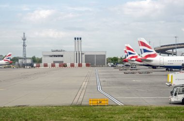 Londra, İngiltere - 19 Nisan 2022: Güneşli bir bahar sabahı Heathrow Havaalanı 'ndaki stantlarında İngiliz Havayolları' nın planladığı ana Terminal 5 binasının yanındaki bacalı bir endüstriyel destek binasının görüntüsü.