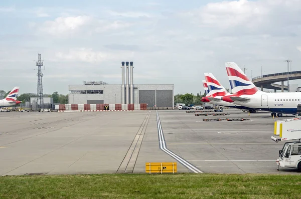 Londra, İngiltere - 19 Nisan 2022: Güneşli bir bahar sabahı Heathrow Havaalanı 'ndaki stantlarında İngiliz Havayolları' nın planladığı ana Terminal 5 binasının yanındaki bacalı bir endüstriyel destek binasının görüntüsü.