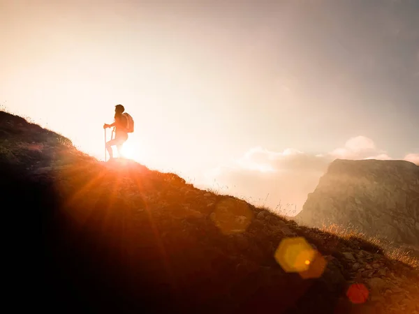 Success symbol. Silhouette of a woman hiking in the mountains at sunset with sun flare. Happiness and freedom.