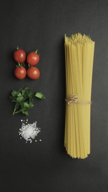 raw spaghetti with tomatoes and basil on black background