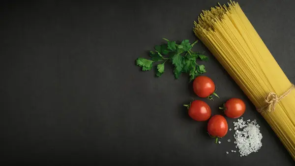 raw spaghetti and vegetables on a black background. top view. free space for your text.