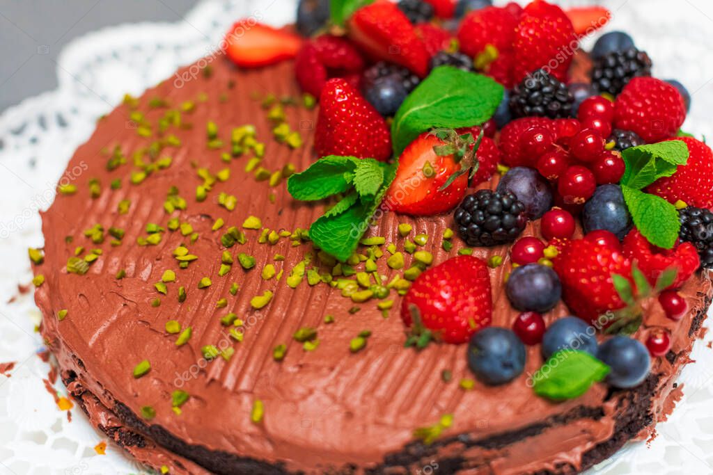 Delicious home made berries decorated vegetarian chocolate cake on white table in the kitchen