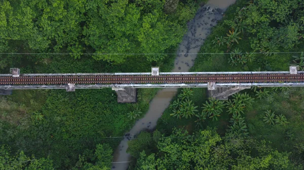 Top down drone shot of train bridge crossing a river near forest in Indonesia on a bright day