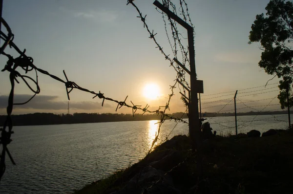 Barbed wire fence and a amazing silhouette sunrise with background mountains and reservoir in Malang, Indonesia