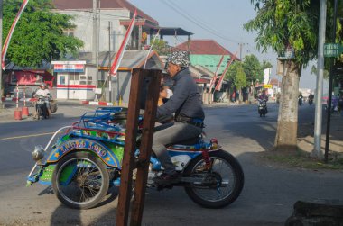 Malang, Endonezya - 4 Eylül 2022: Malang 'da sabah otobandan geçen çocuk taksisi veya triportör sürücüsü