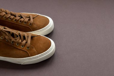 Koyu kahverengi arka planda bir çift kahverengi süet spor ayakkabı. Boşluğu kopyala.