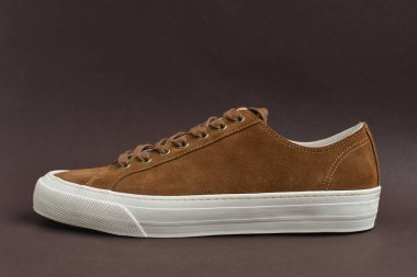 Koyu kahverengi arka planda kahverengi süet spor ayakkabıyı kapat. Boşluğu kopyala.