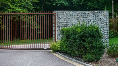 Close up view of entrance to the house in the woods, with modern gates with rust effect and gabion wall.