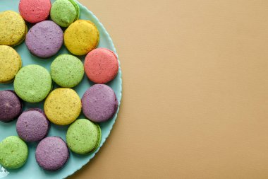 Top view of multicolored macaroons in blue plate on beige background.