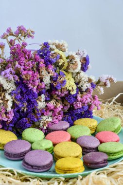 Colorful macaroons on blue plate, decarated with dry flowers, on decorative wood shavings background. Selective focus.