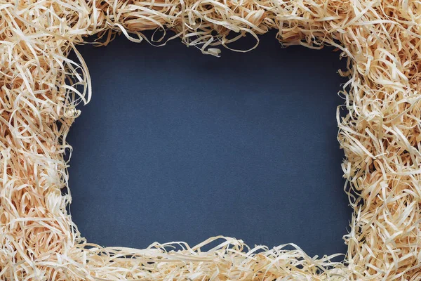 Framework for photo or invitation made of wood shavings on dark grey background. Copy space.