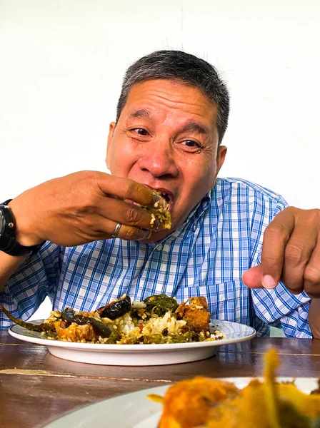 man eating delicious indonesian traditional padangnese food on the white table.