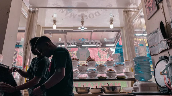 two young man working on a counter of padangnese indonesian restaurant 