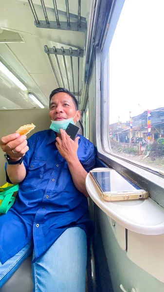 a middle-aged man with a mask is laughing and enjoying food on the Indonesian state train