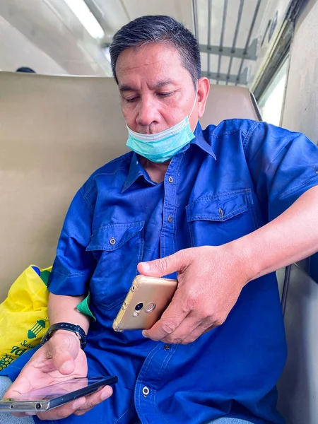 a man in a protective mask is sitting at the table and looking at his smartphone