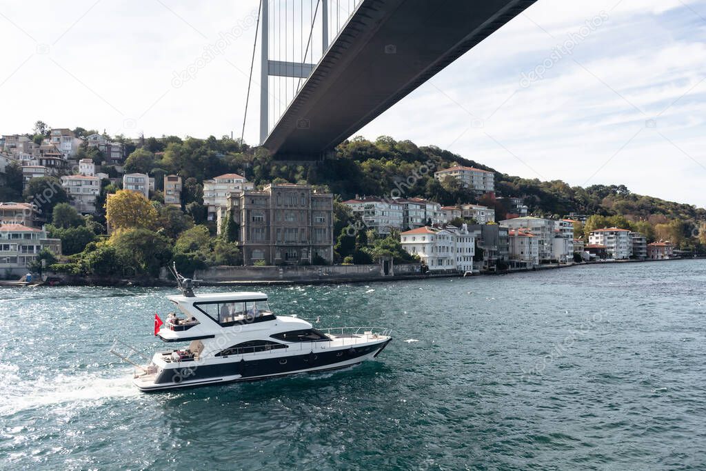 View of a yacht passing on Bosphorus, Rumeli Hisari neighborhood on European side and FSM bridge in Istanbul. It is a sunny summer day. Beautiful travel scene.