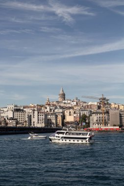 View of a tour boat and yacht on Golden Horn part of Bosphorus in Istanbul. Galata tower and Beyoglu district are in the view. It is a sunny summer day.