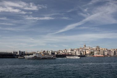 View of a traditional ferry boat and tour boat on Golden Horn part of Bosphorus in Istanbul. Galata tower and Beyoglu district are in the view. It is a sunny summer day.