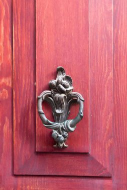Close up view of old, traditional, ornamental door knob on red wood background.