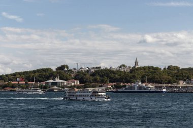 View of Bosphorus tour boats passing in front of Topkapi Palace in Istanbul. It is a sunny summer day.