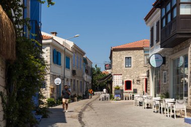 Ünlü, turistik Ege kasabası Alacati 'de eski, tarihi ve geleneksel taş evlerde yürüyen insanları görmek. Bu, Cesme ilinin bir köyüdür. Güneşli bir yaz günü.