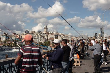 İstanbul 'daki Galata Köprüsü' nde çok sayıda balıkçı görülüyor. Arka planda Galata kulesi ve Beyoğlu bölgesi var. Görüntü, yerel halkın yaşam tarzını ve kültürünü yansıtıyor. Güneşli bir yaz günü..
