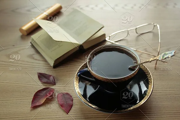 A small volume of a book, a cup of coffee, glasses and three autumn leaves are on the table