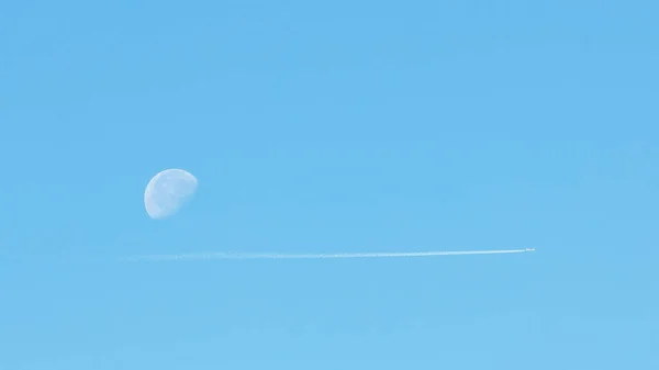Aircraft with white condensing paths. Jet plane on a clear blue sky with a pair of paths. Travel on the concept of an airplane. Traces of exhaust gas from the aircraft engine. Aircraft with white stripes on the background of the Moon