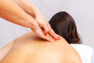 relaxed young woman lying face down on massage table enjoying therapeutic body massage by professional masseur in spa or wellness center.