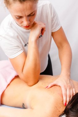 relaxed young woman lying face down on massage table enjoying therapeutic body massage by professional masseur in spa or wellness center.